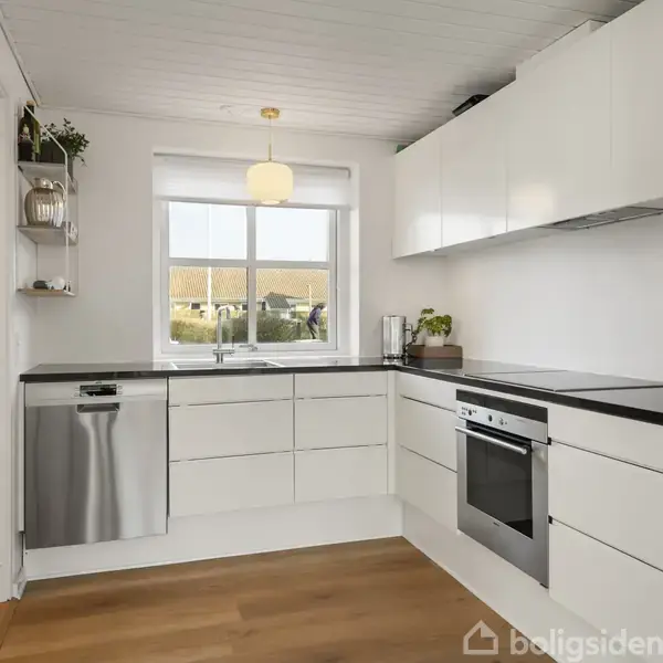 Hvidt, moderne køkken med indbyggede skabe, opvaskemaskine og ovn. En stor, lysende lampe hænger over vasken ved vinduet. Trægulv understøtter en stilfuld og ryddelig atmosfære.