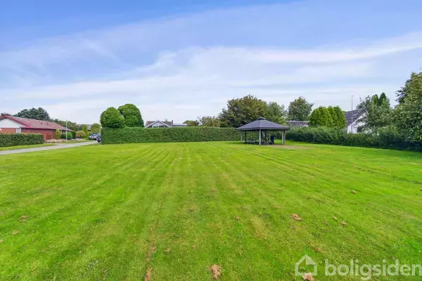 Pavillon står på en velplejet græsplæne omgivet af buske og træer i et fredeligt boligområde.