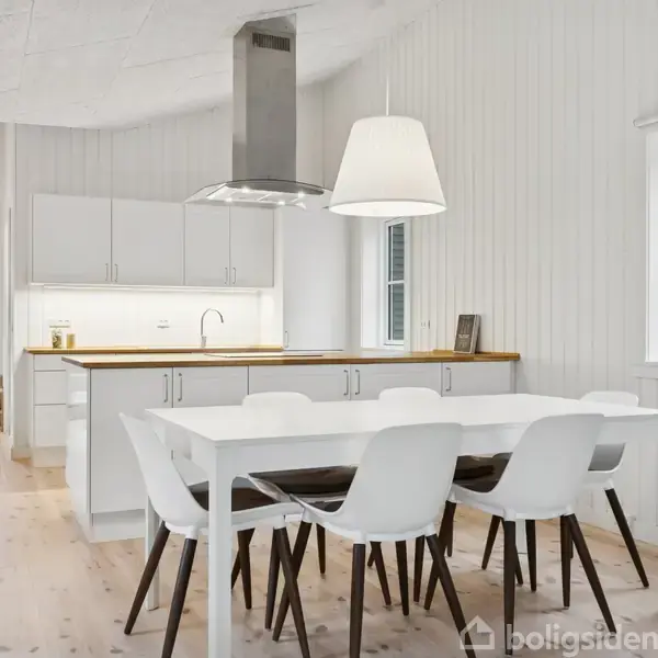 Sofa med puder står ved siden af et sort sofabord med stearinlys. En maleri hænger over sofaen. Store vinduer viser udsigt til terrasse og træer udenfor.