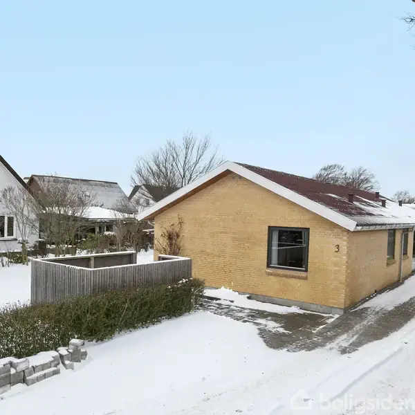 Et gul murstenshus med rødt tag står i et snedækket område. Nummeret 3 er tydeligt på facaden. Husrække og træer omkranser huset, og indkørslen er delvist ryddet.