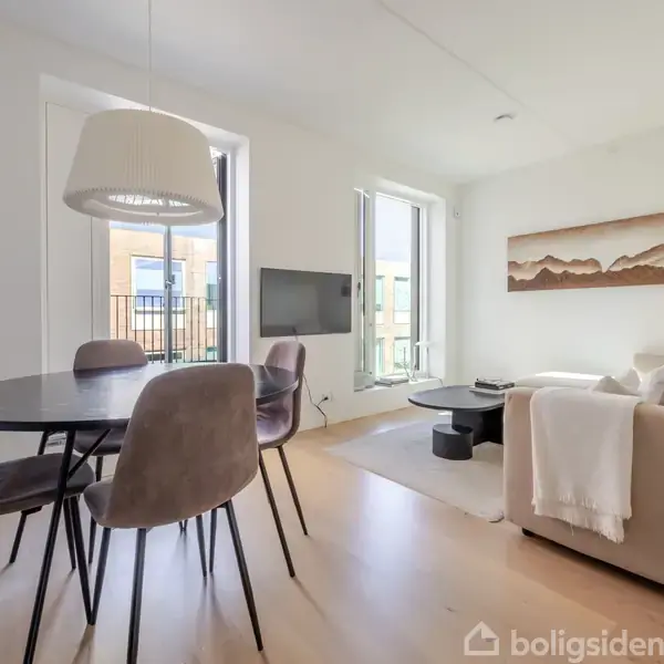 Et moderne stueområde med sofa og kaffebord ved siden af et spisebord med fire stole. Stuen har store vinduer, en vægmonteret fladskærms-TV og et kunstmaleri på væggen.