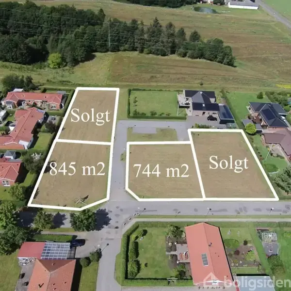 Tre parceller, to markeret som 'Solgt', omgivende huse og grønne områder. De to usolgte parceller er på 845 m2 og 744 m2. Billedet viser en beboelsesgade i et landligt område.
