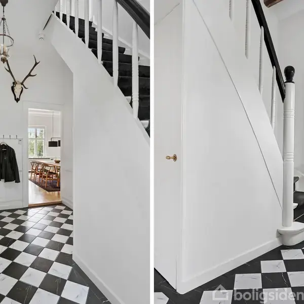 En entré med sort-hvidternet gulv og en trappe med sort gelænder. Der hænger tøj på knager, og en lampe samt gevir pryder væggen. Udsigt til et værelse.