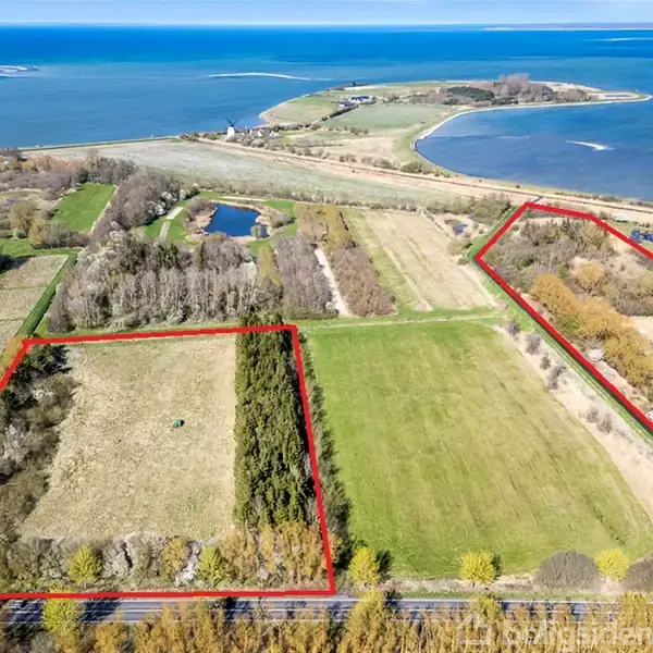 To landområder markeret med røde linjer ligger ved kysten. Det ene område er dækket af træer og åbne marker, mens det andet har mere buskads. Kysten og havet ses i baggrunden.