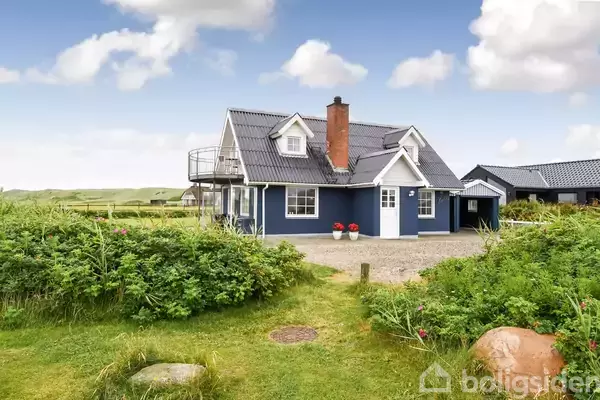 Et blåt hus med hvidt tag står omgivet af grønne planter; i baggrunden ses en blå himmel med skyer og en stor åben græsplæne.