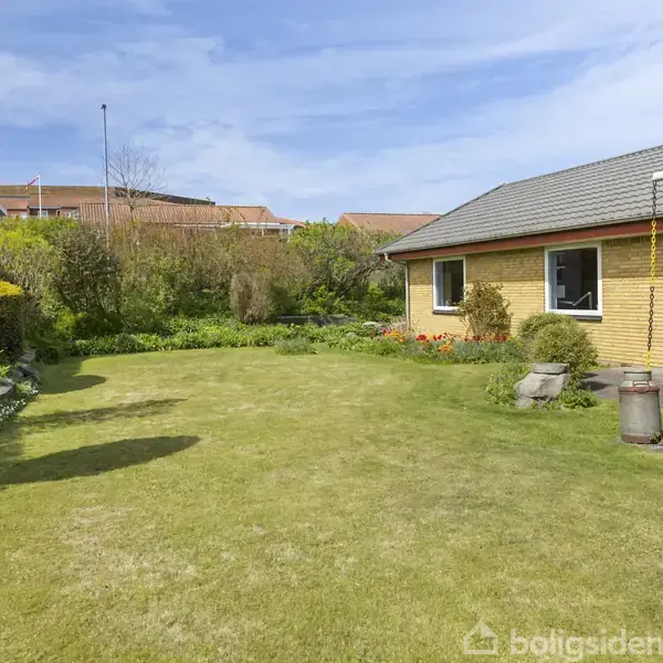 Stue med sorte lædersofaer og borde med planter og lamper, omgivet af store vinduer og gardiner. Lyse vægge og loft, indbydende atmosfære med udsigt til haven.