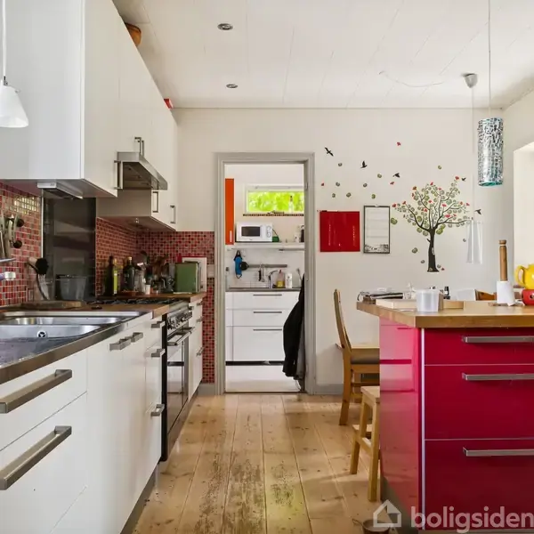 Et moderne køkken med hvide skabe og en rød mosaik-bagvæg. Aktiviteter inkluderer en uordnet køkkenbordplade. Konteksten er lys med træmøbler og ophængt kunst på væggen.