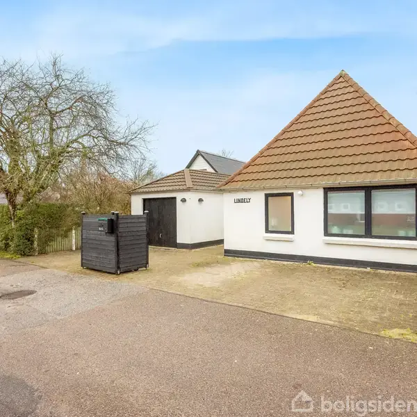 Et hvidt hus med brunt tag står stille på en vej. Huset har store vinduer og en dør til højre. Omkring ses et roligt beboelseskvarter med træer og buske. Texten "Laursens" er på facaden.