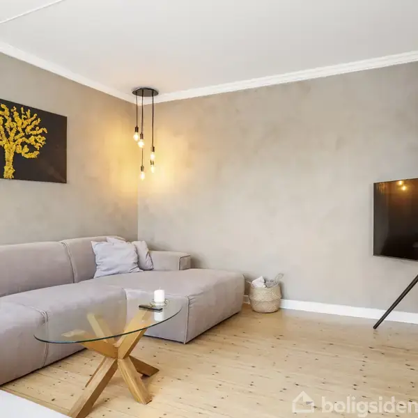 Gråt sofahjørne med glasbord, hængende moderne lyspærer og kunstværk af træer på væggen. Fladskærms-tv står på trefoden. Lyst, trægulv og minimalistisk stil.