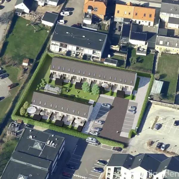 Rækkehuse omgiver en grøn fælles have med stier og træer. Parkeringspladser er i nærheden. Omgivet af andre boligbygninger og gader.