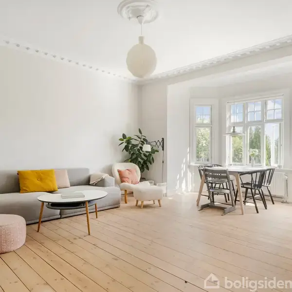 Stue med gråt hjørnesofaarrangement og sofabord, lysindfald fra karnapvinduer, og spisebord med stole til venstre. Trægulv og lyse vægge, minimalistisk indretning.