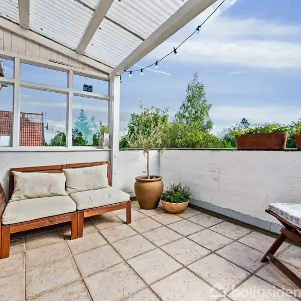 Rundt spisebord med sorte stole står i en lys spisestue, dekoreret med en verdenskort plakat. Til venstre er bogreoler, og til højre ses et køkken i hvidt træ.