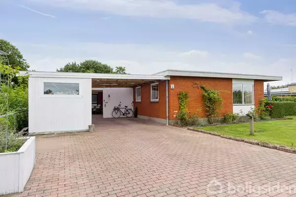 En etplans villa med fladt tag; cykel parkeret i carport; omgivet af græsplæne og blomstrende buske på roligt villavejsmiljø.