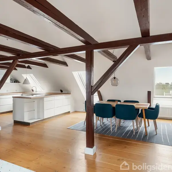 En elegant trappeopgang med lygtestander og messinggelænder fører op til en korridor. Ovenfor hænger moderne lysekroner, og en plante står ved siden af foran en buegang.