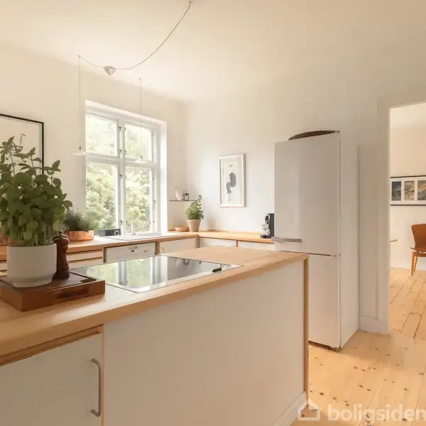 Et lyst køkken med træbordplade og indbygget kogeplade. Planter og rammer pryder vindueskarmen. Til højre ses en åbning til et rum med trægulv og stol.