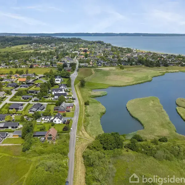 En landsby ved en sø, omgivet af marker og grønt landskab. Søen har elliptiske øer. Husene danner rækker langs veje, og landsbyen ligger tættere på horisonten.