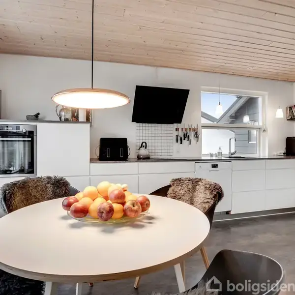 Et snedækket græsareal med et stort træ står i haven. En stige og et gyngestativ er ved siden af huset. En træterrasse ses i baggrunden.