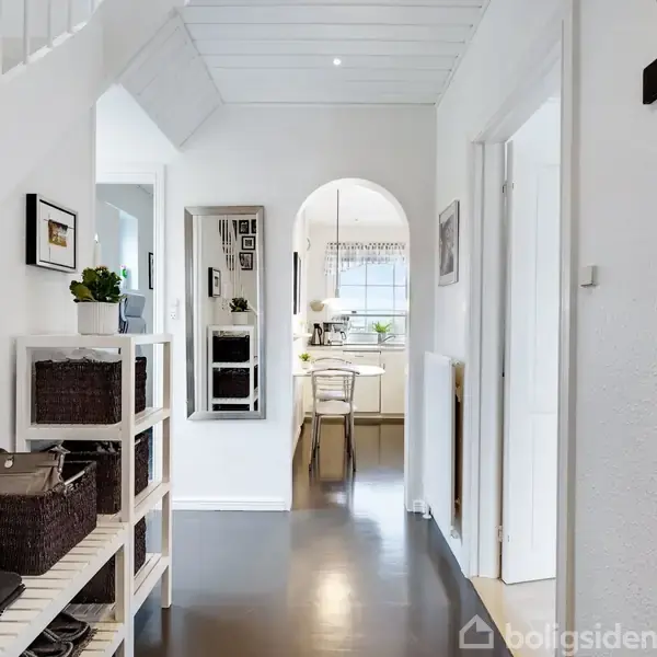Et rødt hus med sort tag står ved siden af en carport. Omgivet af hække og en flisebelagt indkørsel, ses det fra en gade i et boligområde.