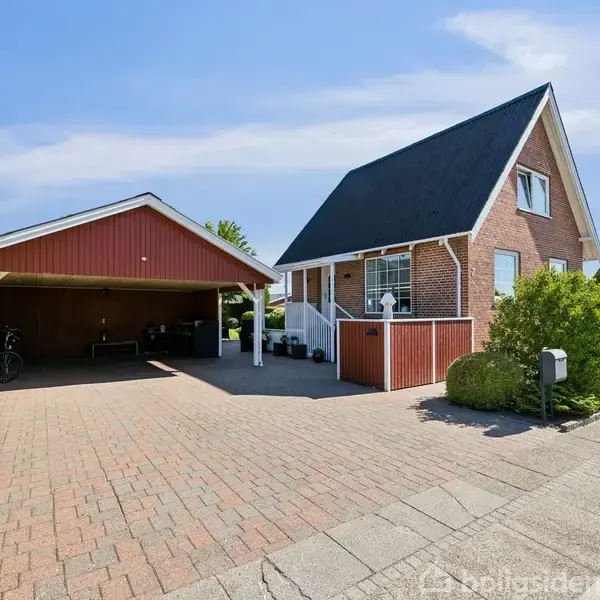 En lys entre med flethylder og kurve. Gangen fører til et køkken gennem en buet døråbning. Væggene er hvide, og gulvet er skinnende.