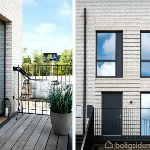 Balkon med træplanker og havemøbler står udenfor en bygning af lyse mursten med store vinduer. Grønne planter omgiver området, mens himlen er blå med få skyer.