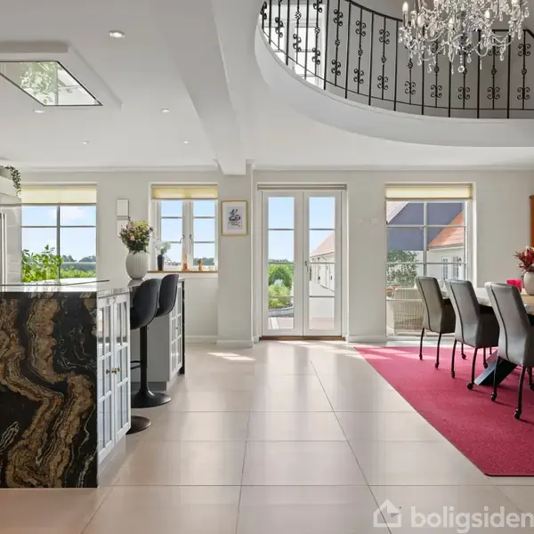 Køkken-alrum med stor spisebord, læderstole og elegant lysekrone. Køkkenø med marmorbordplade, stående barstole og moderne apparater. Franske døre fører til lysfyldt terrasse med udsigt.