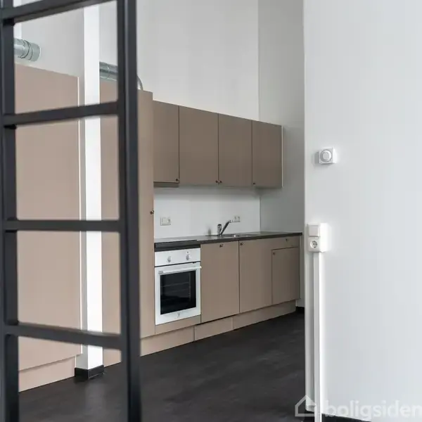 Et moderne køkken med lysebrune skabe og en indbygget ovn. Handlingen er stationær. Konteksten viser en delvist synlig stige og hvide vægge i et minimalistisk rum.