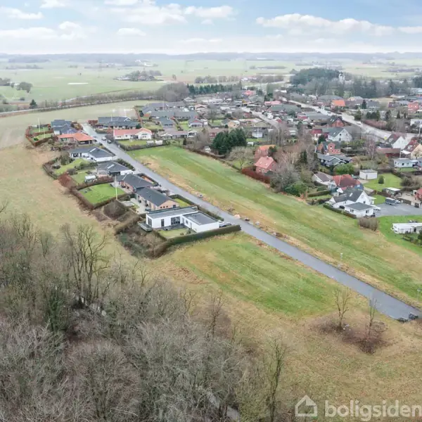 Boligområde set fra luften. Række af moderne huse med veje beliggende ved siden af marker og skov. Omkringliggende landskab viser en bred udsigt af marker og beboelsesområder.