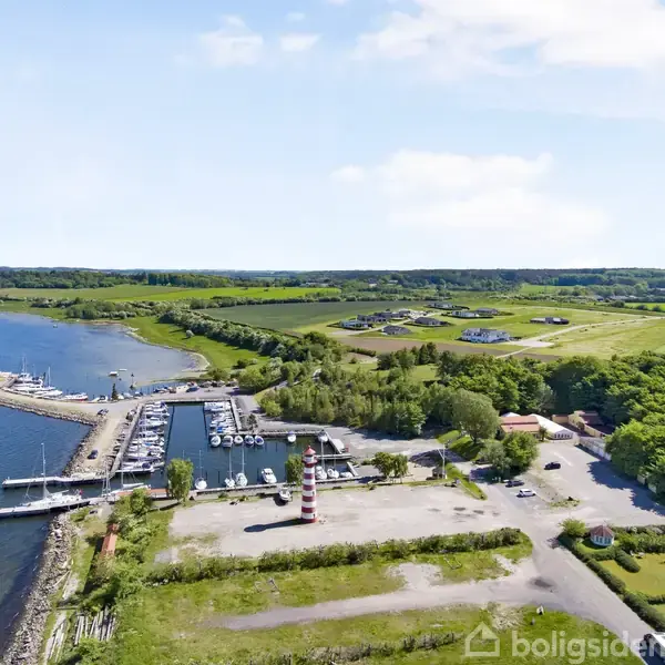 En marina med både ligger stille ved vandet; omkringliggende grønne marker og skove danner en landlig, fredfyldt atmosfære. Der er ingen tekst i billedet.
