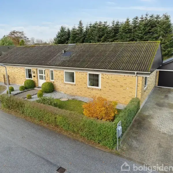 Gulstenshus står i en forstadsgade med indkørsel og garage. Haven har velplejede buske og træer. Huset har flere vinduer og et mørkt tag, omgivet af grønne hække.