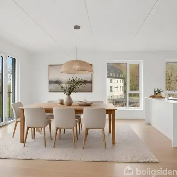 Spisebord med seks stole står i et lyst køkken-alrum. Bordet er pyntet med planter i en vase. Store vinduer og en altandør giver udsigt til et grønt område. Tekst: "Visualisering".