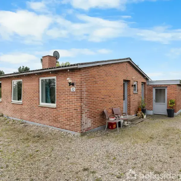 En rødstensvilla står stille i en åben grusbelagt have. Tre vinduer er synlige, med nummer "10" ved døren. En stol og nogle planter ses ved indgangen.