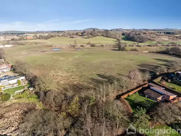 Sø omgivet af beboelsesområde; huse omringer søen fra flere sider, mens åbne marker ses i forgrunden og resten af byen strækker sig i baggrunden.