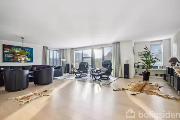 En moderne stue har sorte lænestole og sofaborde på et tæppe. Store vinduer lukker lys ind, omgivet af malerier, potteplanter og skind på trægulvet i et stilfuldt interiør.