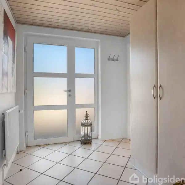 Dør med glasruder står i en entré med flisegulv. Et skab og et billede hænger på væggen. En lanterne er placeret foran døren. Vægge og loft er hvide.