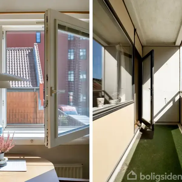 Et åbent vindue med udsigt til hustage ved et bord med planter og en lampe. Ved siden af en balkon med grønne gulvtæpper under blå himmel.