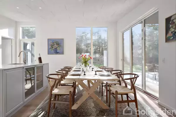 Udendørs bruser af metal sprøjter vand, monteret på en sort trævæg. En lampe er synlig over bruseren, og himlen er blå i baggrunden.