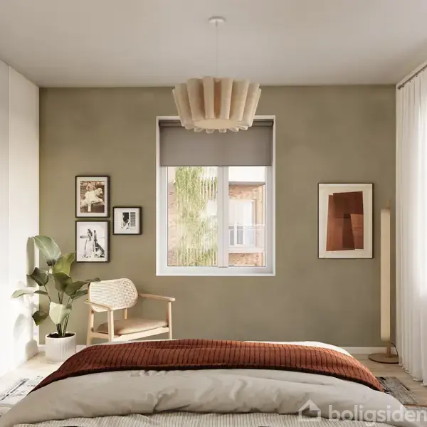 Soveværelset har en seng med brun plaid, en moderne stol, planter og billeder på væggen. Store vinduer lader lys ind, og garderobeskabe er langs den ene væg.