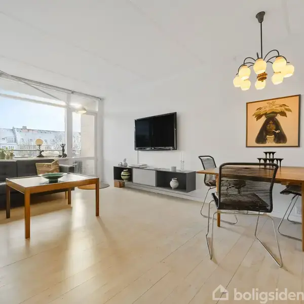 Stue med sofa og sofabord ved store vinduer, fjernsyn på væggen, spisestue med bord og fire stole under hængelampe, lyst trægulv, kunstbillede på væggen.