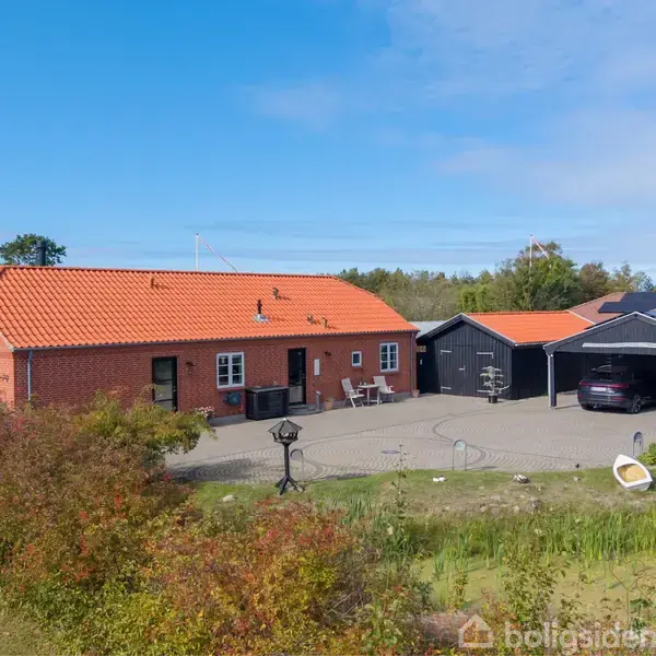 Rødt murstenshus med orange tegltag står i en have. Til højre er en garage med en parkeret bil. Blå himmel og grønne buske omkranser ejendommen.
