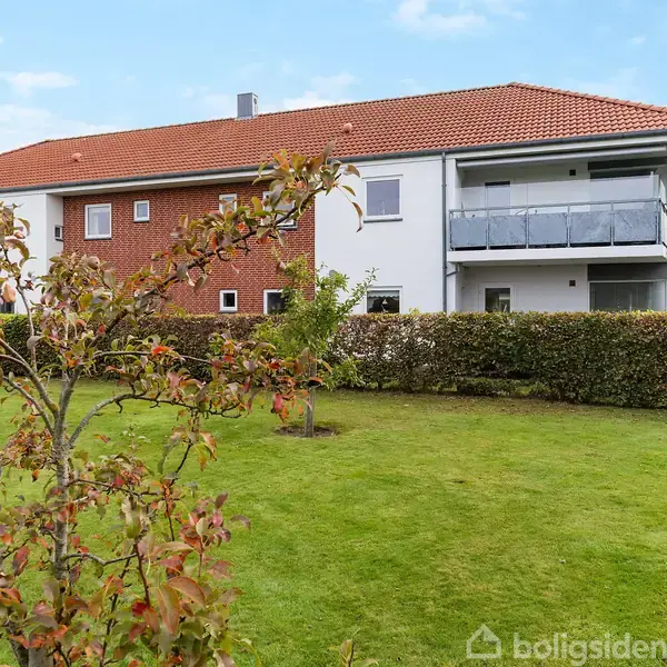 En stue med en stribet sofa og en grå lænestol, placeret nær et stort vindue. Der er et spisebord med stole, en skænk og billeder på væggen.