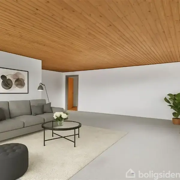 Grå sofa står i stue med lys træloft. Ved siden af er et rundt bord med blomster og en sort skammel. Billedet på væggen viser abstrakt kunst. En plante står i hjørnet ved brændeovn.