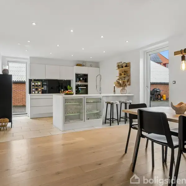 Køkken, moderne stil, med hvidt bord, indbygningsskabe, og sort spisebord med fire stole. Væggene har dekorative elementer, og der er en rude til venstre med udsigt til en gård.