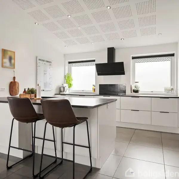 Spisebord med gennemsigtig dug og vase med blomster, omgivet af sorte stole. Loftlamper hænger over bordet. Terrassedøre åbner ud til en have med beplantning.