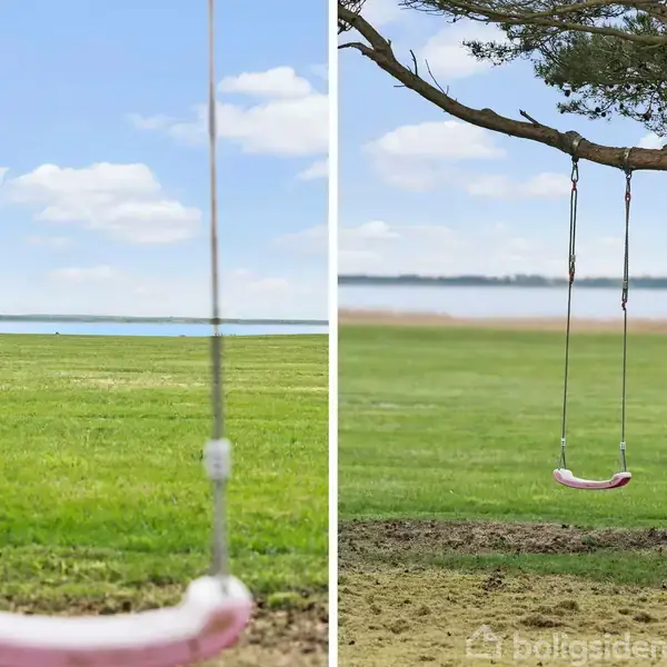 En gynge hænger stille fra et træ. Omgivelserne består af en grøn græsplæne ved siden af vand med en blå himmel i baggrunden.