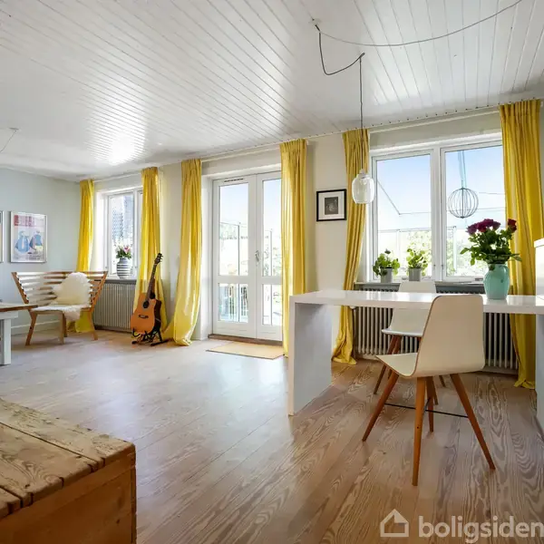 Lyse og rummelige stue med træmøbler, parketgulv og gule gardiner. En guitar står ved vinduet, mens planter pynter på bordet ved franske døre, hvilket skaber en behagelig atmosfære.