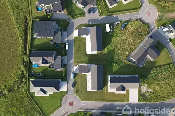 Luftfoto af et boligområde med seks huse, der er placeret langs veje med grønne haver imellem. Husene er moderne, og vejene danner et netværk gennem kvarteret.