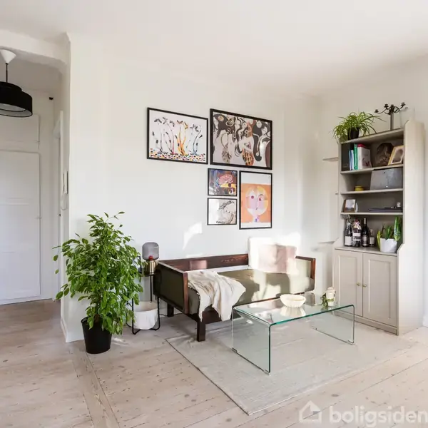 Stue med glasbord og træsofa, omringet af kunstværker på væggen. Reol med bøger og planter i hjørnet. Skilt siger "LES FLEURS". Lysindfald fra venstre.