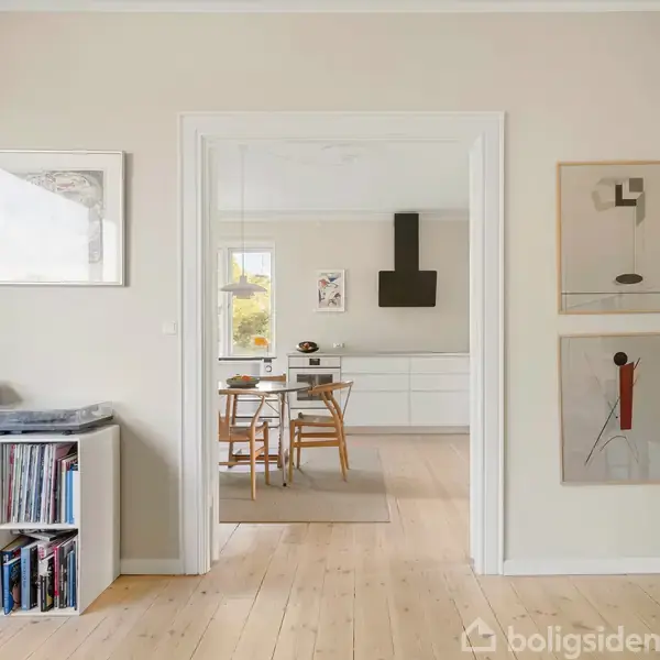 Reol fuld af plader står stille ved væggen i en lys stue. Gennem en dør ses et køkken med bord og stole. Malerier hænger på væggen.