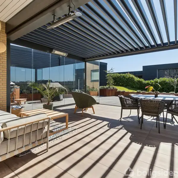 Terrasse med moderne møbler under en pergola; sofa og bord til venstre, spisebord med stole til højre. Glaspaneler omgiver området, med udsigt til en frodig have.