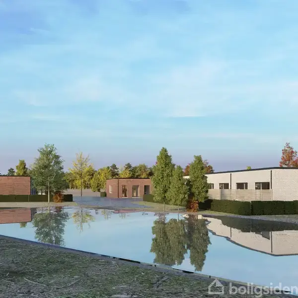 Flade, moderne huse reflekteres i en stor, rolig vandflade. Træer og buske omgiver området, og himlen er blå med lette skyer.